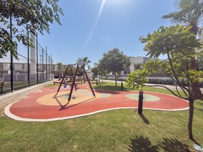 A playground with swings and a red and green play area, surrounded by a fence and trees. - Vogue, Wadi Al Safa Villa The Fields Elie Saab (Wadi Al Safa)