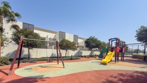 Ein Spielplatz mit Schaukeln und Rutsche, umgeben von einem Gebäude und Bäumen.
