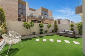 Ein modernes Gebäude mit flachem Dach, großen Fenstern und einer Dachterrasse mit Kunstgrras und weißen Stühlen.