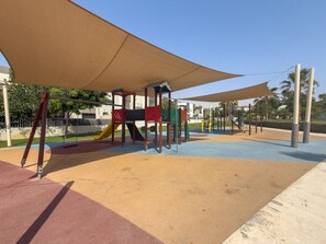 Ein Spielplatz mit Rutsche, Klettergerüsten und schattigen Bereichen.