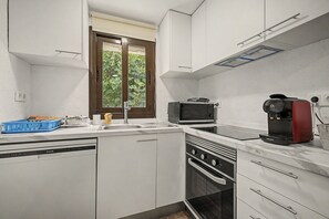 Ett kompakt kök med vita skåp, en inbyggd ugn, en mikrovågsugn och en kaffebryggare.
