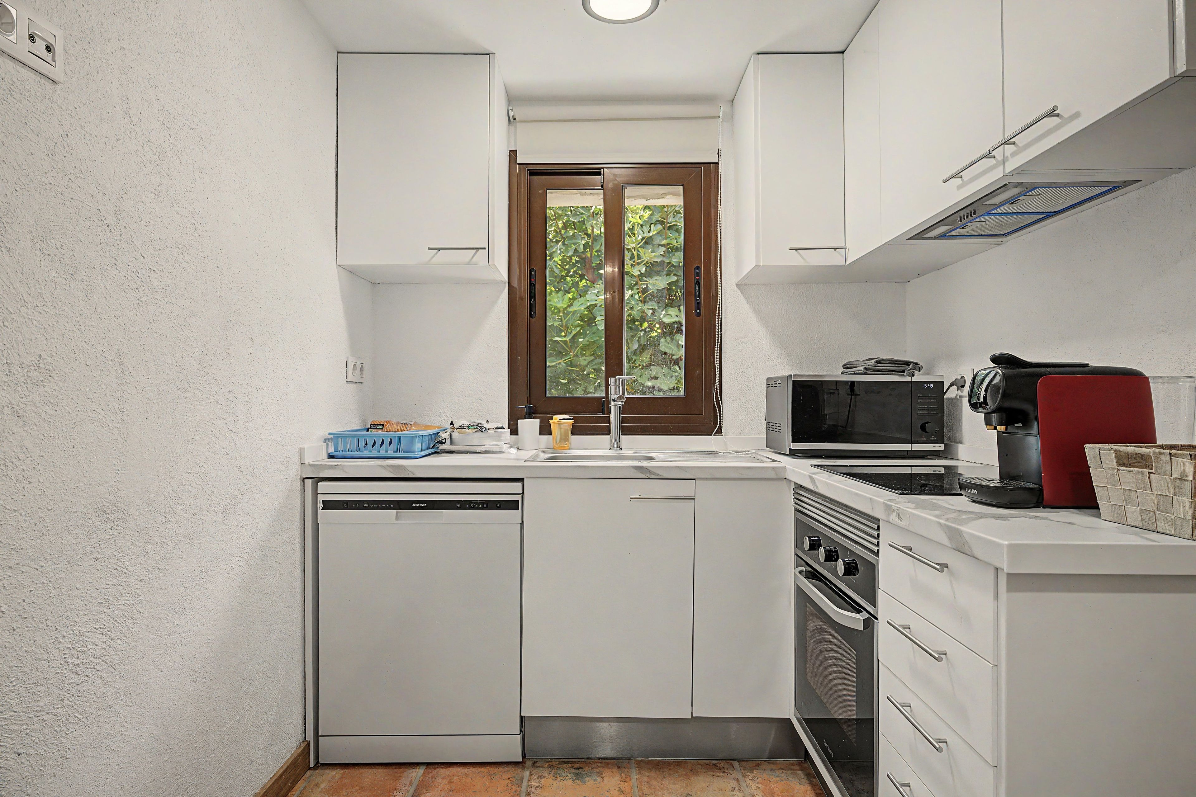 Cozinha compacta com armários brancos, lava-louças, micro-ondas e máquina de café.