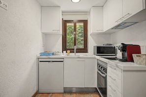 Cocina compacta con armarios blancos, lavavajillas, microondas y cafetera.