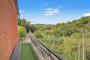 Un balcón con barandilla metálica que da a un paisaje verde con árboles y colinas.