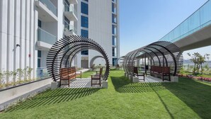 A modern outdoor area with circular metal structures, benches, and a grassy lawn. - Vogue, Arjan Skyz by Danube near Dubai Miracle Garden (Arjan)