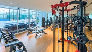 A gym with weightlifting equipment, benches, and a view of the outside. - Vogue, Arjan Skyz by Danube near Dubai Miracle Garden (Arjan)