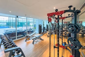 Ein Fitnessraum mit Krafttrainingsgeräten, Bänken und Blick ins Freie.