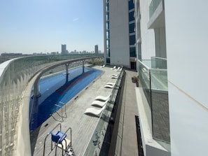 Ein Pool auf dem Dach mit Liegestühlen, einer Glasbrüstung und Blick auf die Skyline der Stadt.
