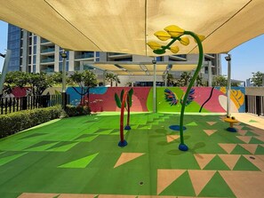 Ein Spielbereich im Freien mit bunten Wandmalereien, einer beschatteten Markise und geometrischen Mustern auf dem Boden.