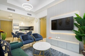 Ein modernes Wohnzimmer mit Fernseher, Sitzgelegenheiten und einer Küche im Hintergrund.