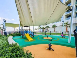 A playground with slides and exercise equipment, surrounded by greenery and a covered area. - Vogue Business Bay Aykon City near Metro Station (Business Bay)