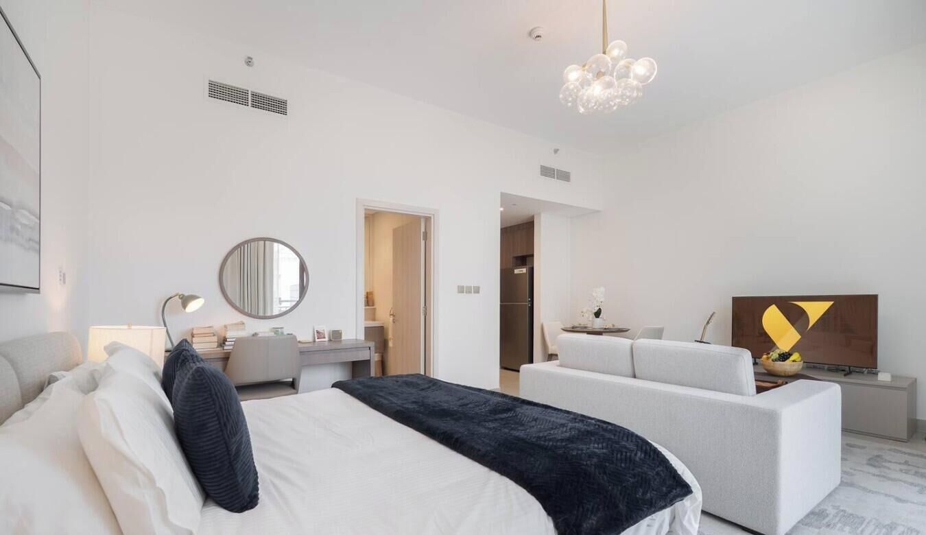 Ein modernes Hotelzimmer mit einem Bett, einem Schreibtisch, einer Sitzecke und einem Fernseher, darüber eine Kristallleuchter.