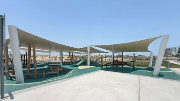 Un patio de juegos al aire libre con estructuras para escalar y zonas con sombra.