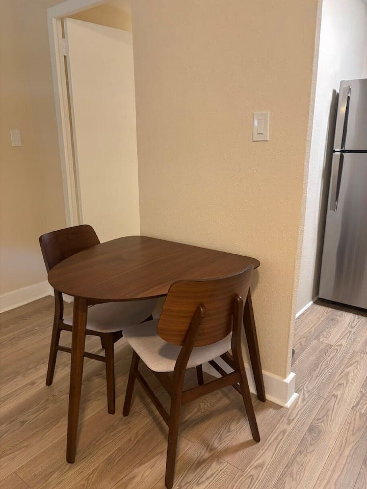 Un coin repas avec une table et des chaises en bois, un réfrigérateur et une porte donnant sur une autre pièce.