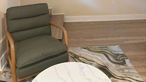 A living room with a flat-screen TV mounted on the wall, a green upholstered chair, and a patterned rug on the wooden floor. - 2 Bedroom Poolside Escape Near Austin Hotspots (Austin)