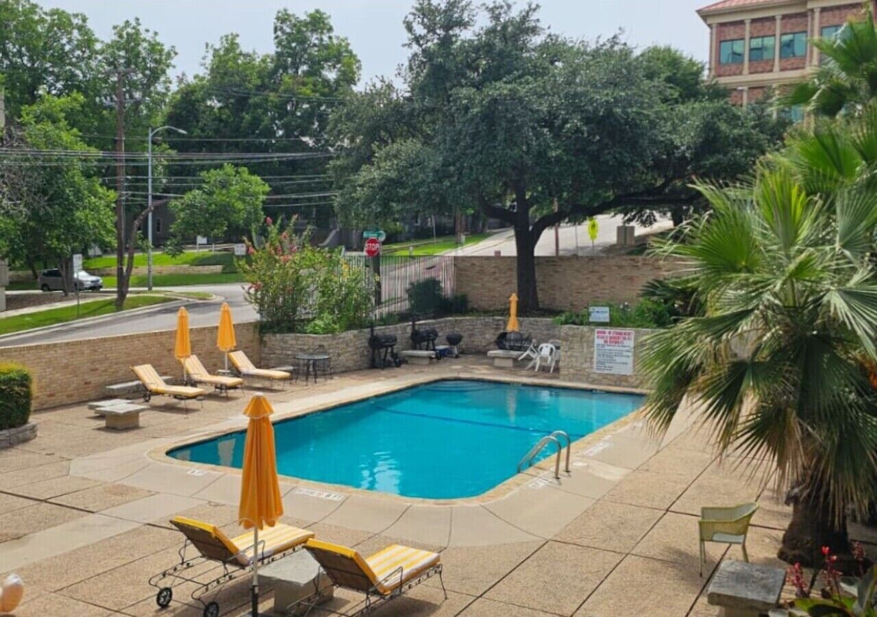 Une piscine rectangulaire, bordée d’une terrasse carrelée, entourée de chaises longues et de parasols.