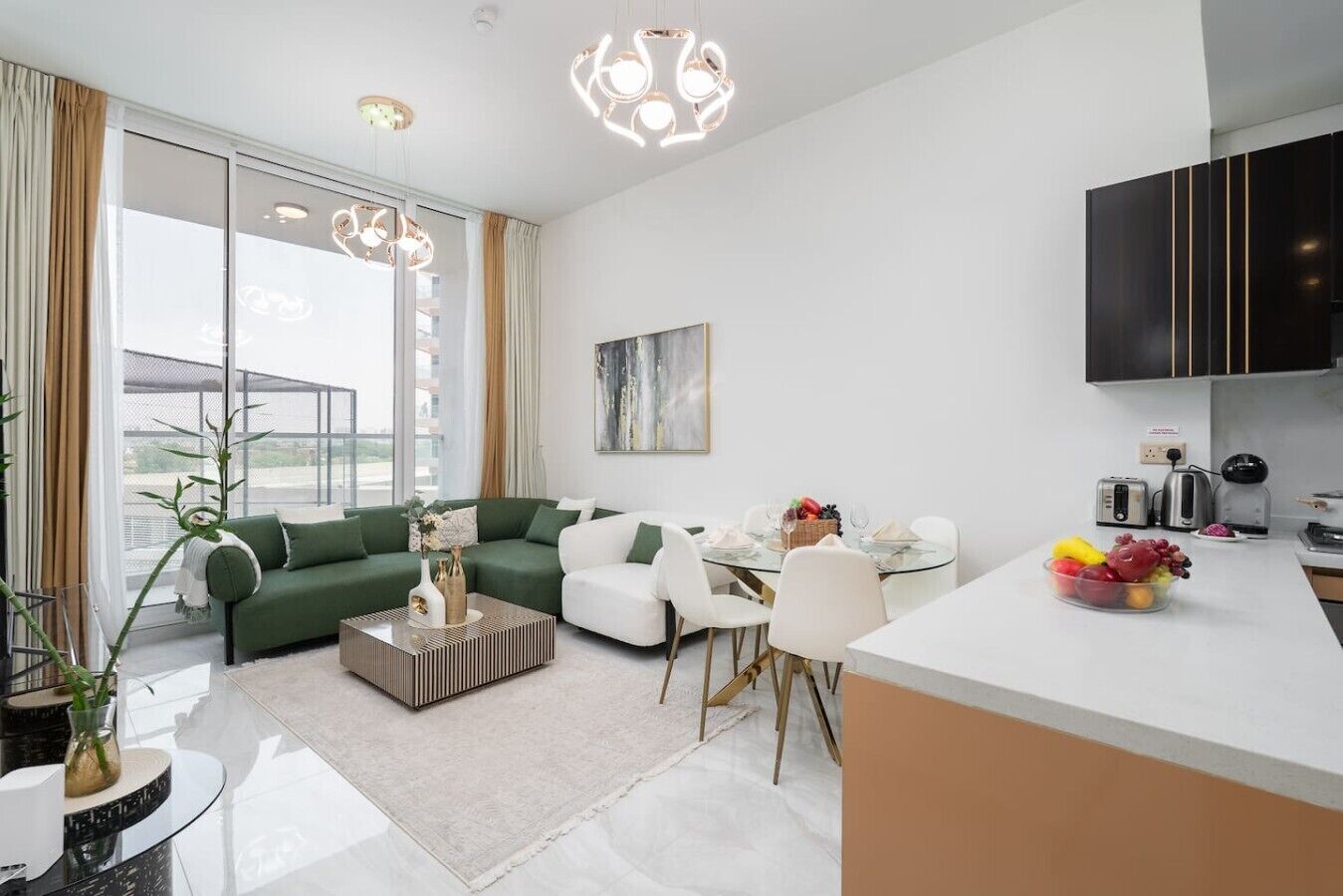 Ein modernes Wohnzimmer mit einem grünen Sofa, einem Glastisch und einem Essbereich mit einem Glastisch. Es gibt eine Küche mit einem schwarzen Schrank und einer Obstschale auf der Arbeitsplatte.