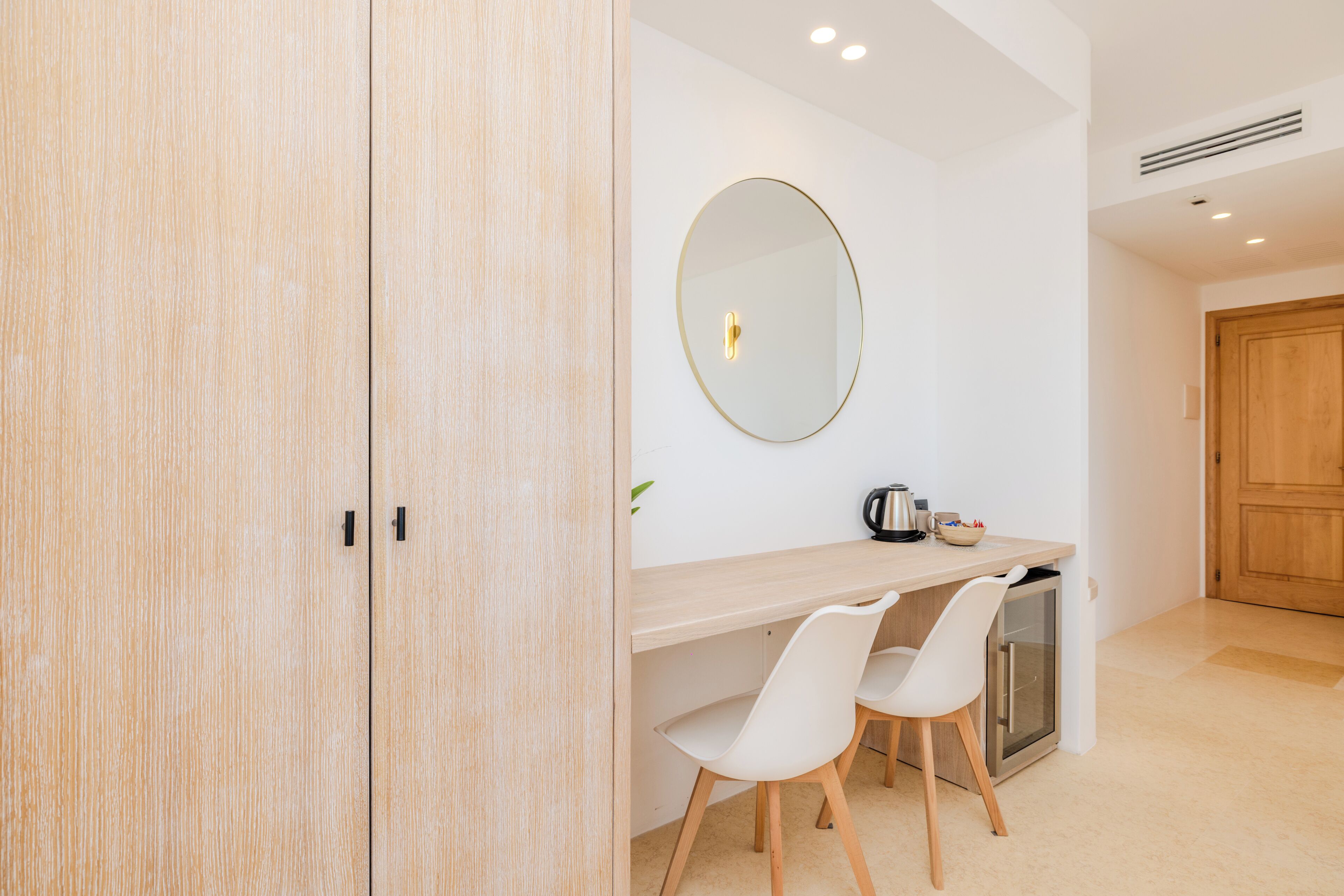 A modern kitchen with a wooden cabinet, a round mirror, a countertop, and two white chairs.