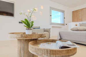 Un dormitorio moderno con cama, ventana, orquídea en maceta y una mesa redonda de madera con una revista.