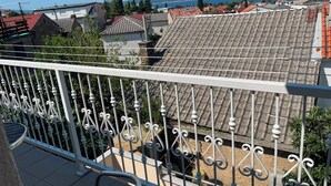 Un balcone con ringhiera bianca, vista sui tetti in tegole rosse e un corpo d'acqua in lontananza.