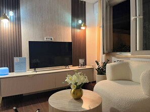 A modern living room with a flat-screen TV, a round coffee table with a vase of flowers, and a sofa.