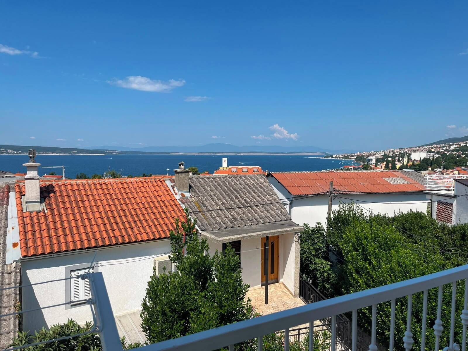 A coastal residential area with terracotta-tiled roofs, white walls, and a clear view of the sea.
