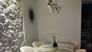 Zona pranzo con un tavolo rotondo, sei sedie, un vaso con fiori, una parete con decorazione strutturata e una lampada a soffitto.