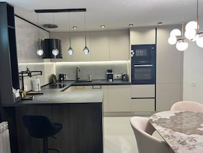 Eine moderne Küche mit Kochinsel, Pendelleuchten, Backofen und Essbereich inklusive Tisch und Stühlen.