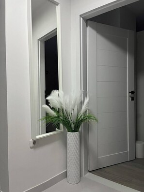 A white door with a handle and a keyhole, a white textured planter with green foliage, and a white wall with a window.