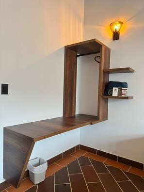 A corner with a wooden bench, a wall-mounted shelf with a cushion, and a wall sconce.