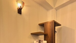 A corner with a wooden shelf unit, a trash bin, and a wall-mounted light fixture. - Hotel Cala (Cucaita)