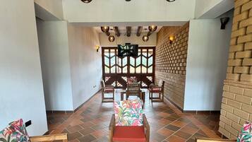 Um hall amplo com uma mesa de centro de madeira, cadeiras estofadas vermelhas e uma parede de tijolos.