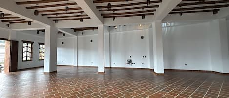 Un interior espacioso con suelo de ladrillo, paredes blancas y vigas de madera a la vista.