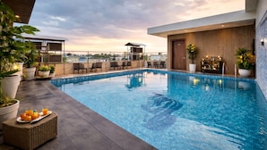 A rooftop pool with lounge chairs, potted plants, and a bar area.