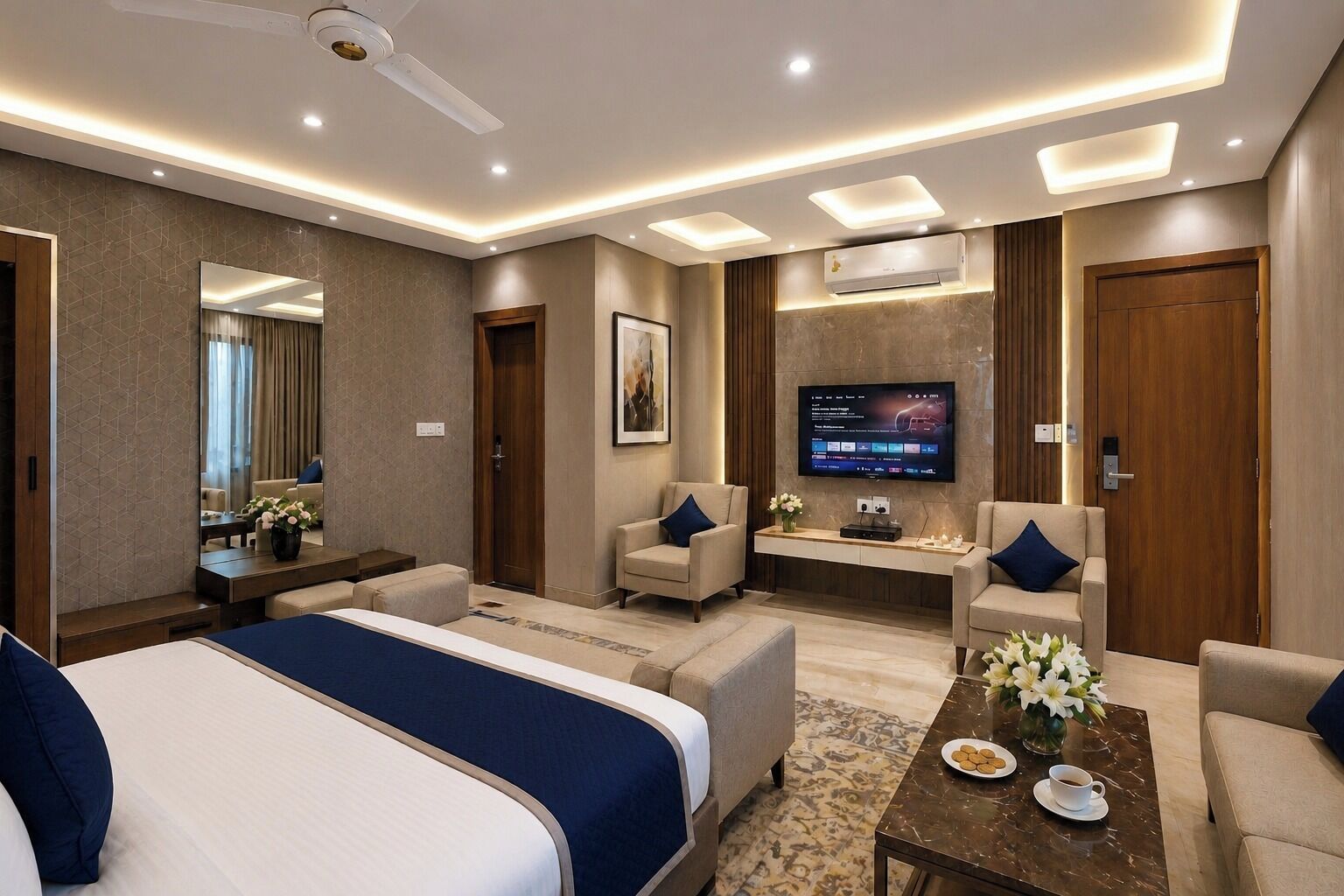 Habitación de hotel con una cama grande, dos sillones, una mesita de centro, un televisor y un escritorio con espejo.