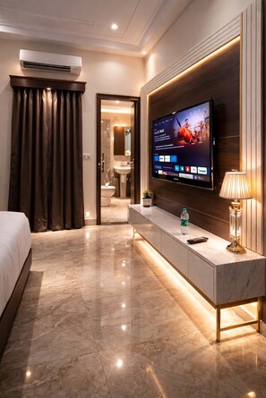 A hotel room with a flat-screen TV mounted on the wall, a bedside table with a lamp, a water bottle, and a remote control. - The Amar Singh Place By Signature Stayz (Agra)