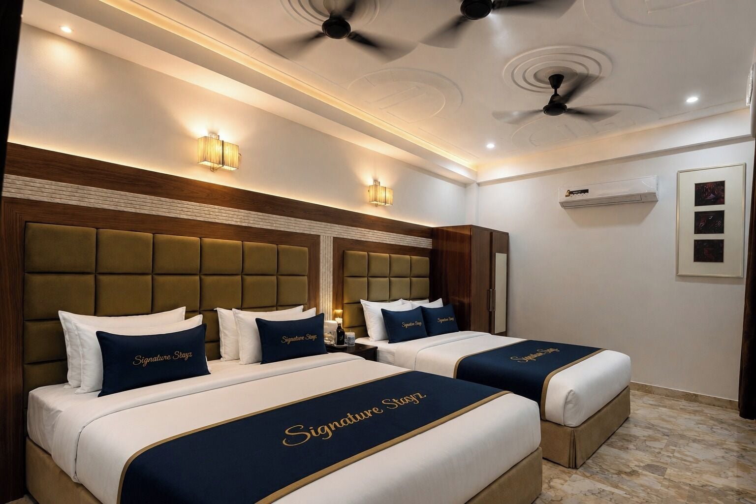 A hotel room with two beds, each with a headboard and a signature-themed bedspread.
