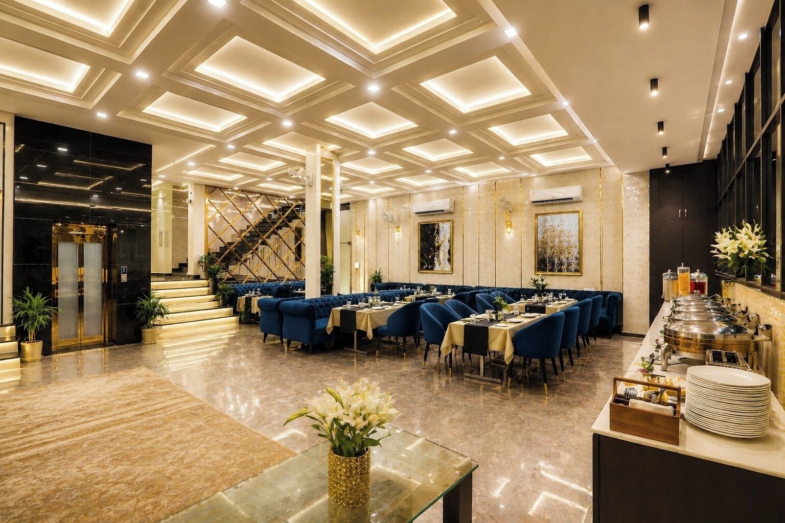 Een hotelhal met een marmeren vloer, een trap, blauwe zitplaatsen en een buffetgedeelte.