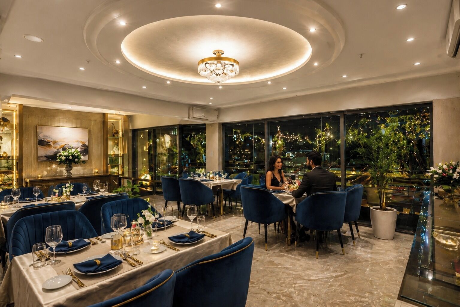 A dining area with tables set for two, a chandelier, and a view of the night sky.