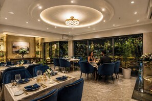 A dining area with tables set for two, a chandelier, and a view of the night sky. - The Amar Singh Place By Signature Stayz (Agra)