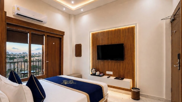 A hotel room with a bed, a TV mounted on a wooden panel, a balcony with a city view, and an air conditioning unit.