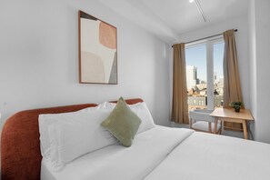 Ein Hotelzimmer mit Bett, Schreibtisch, Stuhl, einem Fenster mit Vorhängen und Blick auf die Stadt.