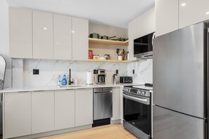 Eine moderne Küche mit weißen Schränken, einem Edelstahlkühlschrank, einem Einbauofen und einer Kaffeemaschine.