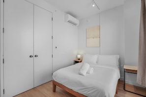 Un dormitorio moderno con cama, mesita de noche, aire acondicionado y un cuadro en la pared.