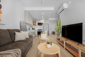 Ein modernes Wohnzimmer mit Sofa, Couchtisch, Fernseher und einer Küche im Hintergrund.