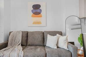 Ein modernes Wohnzimmer mit einem grauen Sofa, einer weißen Tagesdecke und einem schlichten Wandbild.