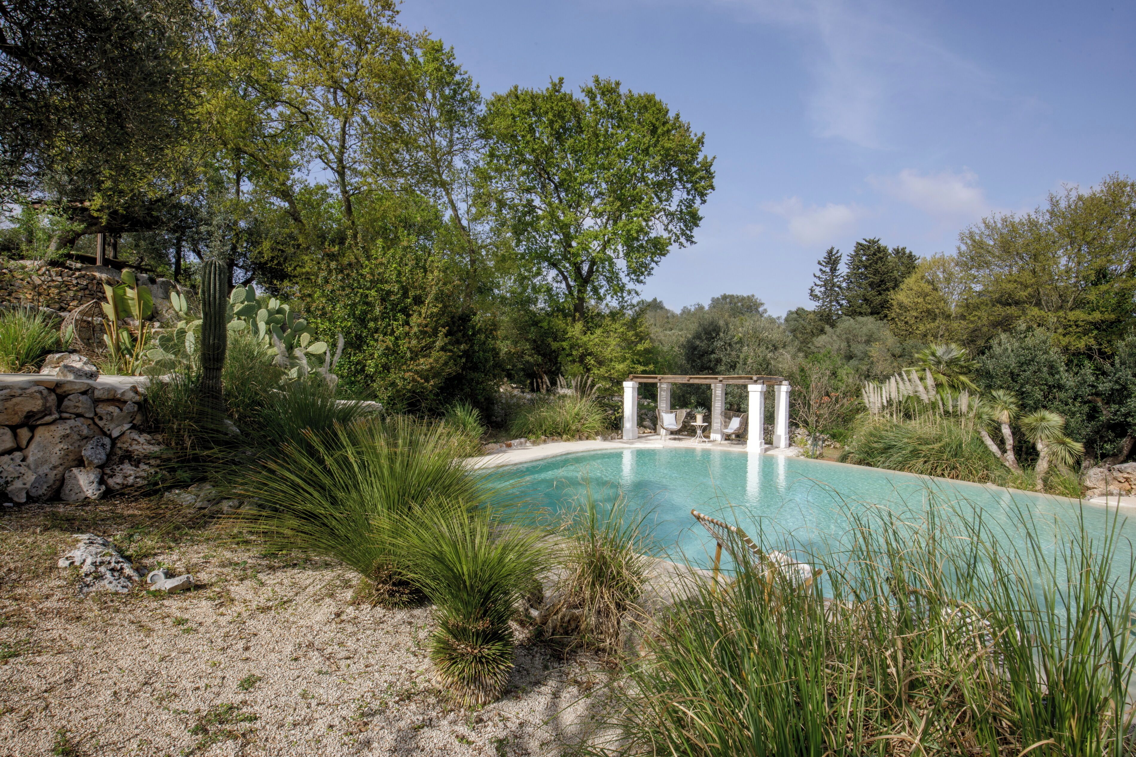 Una piscina rodeada de vegetación natural y un muro de piedra.