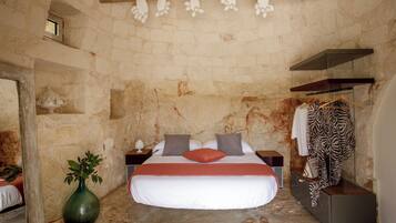 A bedroom with a stone wall, a bed with white bedding and a red pillow, a green vase, and a zebra print garment on a hanger.