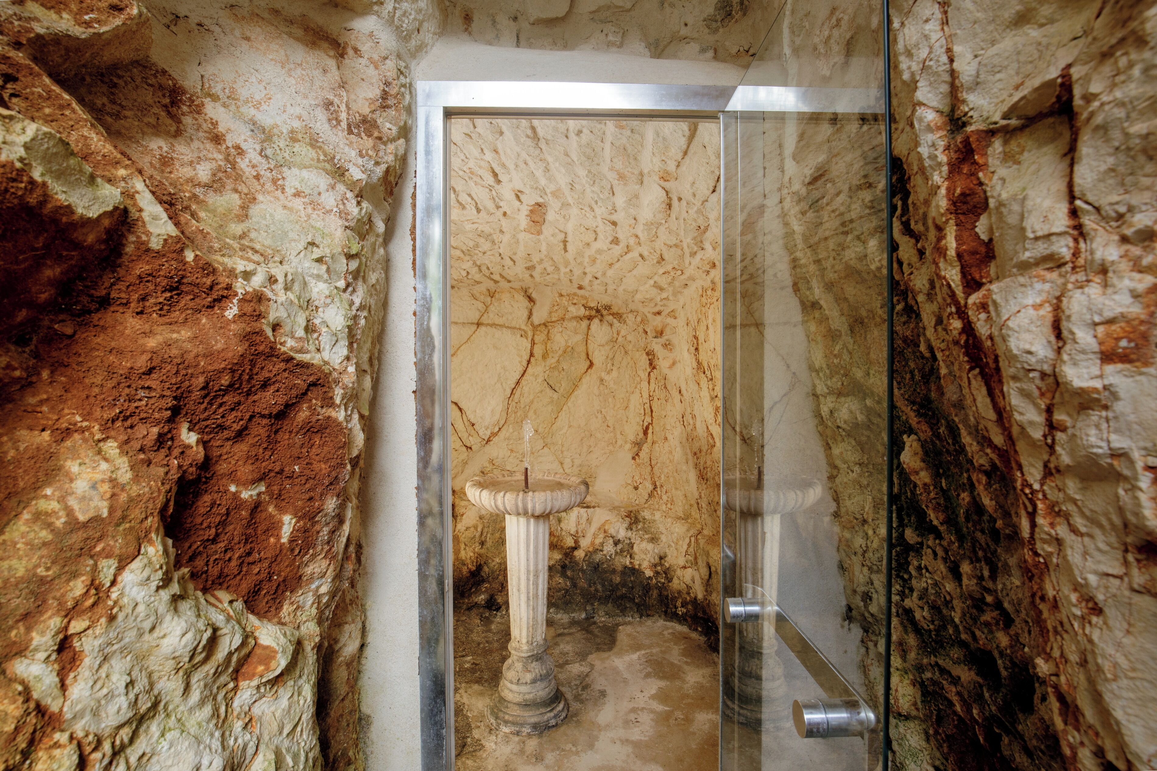Un baño con pared de mármol, lavamanos pedestal y cabina de ducha de vidrio.