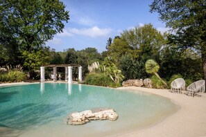A clear pool with a rock feature, surrounded by white chairs and a pergola. - Puntebianche Resort by Hannah Hotels Collection (Ceglie Messapica)